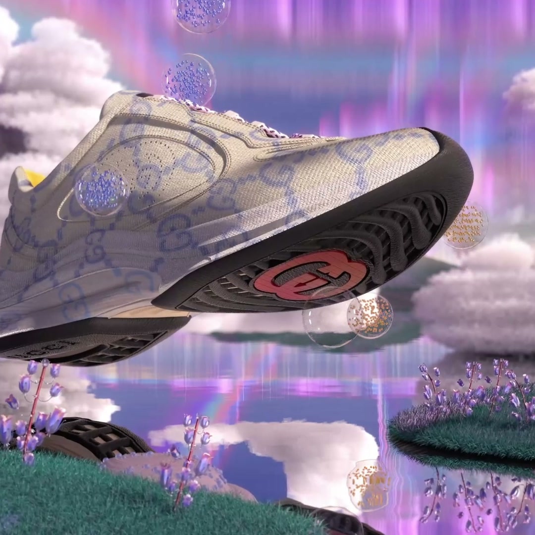 The monogram sneaker tilted in mid-air above a pastel landscape of water, grass tufts and cloud.