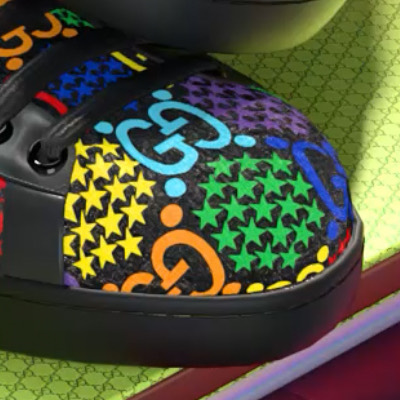 Macro on the toe of a black sneaker, the monogram and stars reading clearly against a green monogram wall.