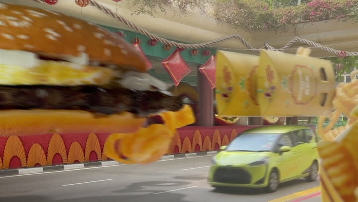The burger travelling above a green car on a decorated street.